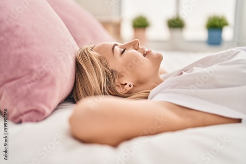 Young blonde woman lying on bed sleeping at bedroom