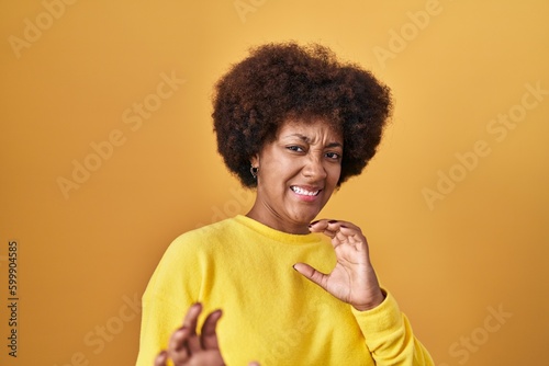 Fotografie, Obraz Young african american woman standing over yellow background disgusted expression, displeased and fearful doing disgust face because aversion reaction