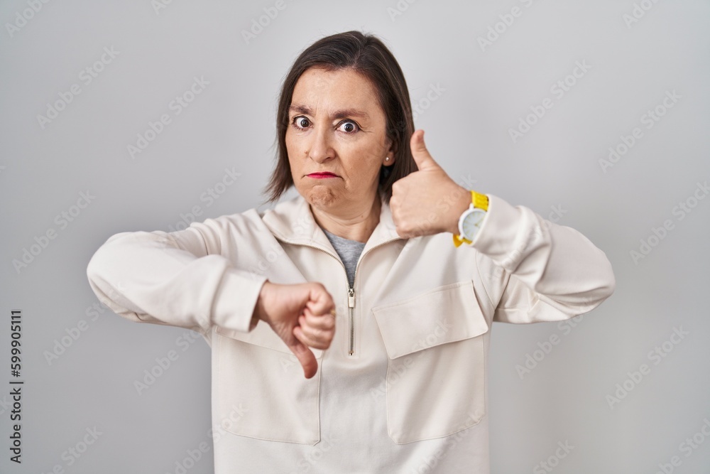 Middle age hispanic woman standing over isolated background doing thumbs up and down, disagreement and agreement expression. crazy conflict Middle age hispanic woman standing over isolated background doing thumbs up and down, disagreement and agreement expression. crazy conflict