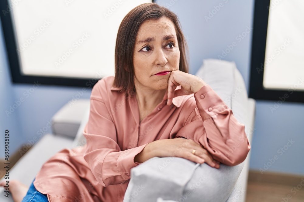 Middle age woman with sad expression sitting on sofa at home Middle age woman with sad expression sitting on sofa at home