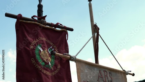 Historical flags of ancient Roman legionaries and gladiators with symbolic design and inscription, two flags hanging on wooden stick and waving against blue sky background, flags called vexillum being photo