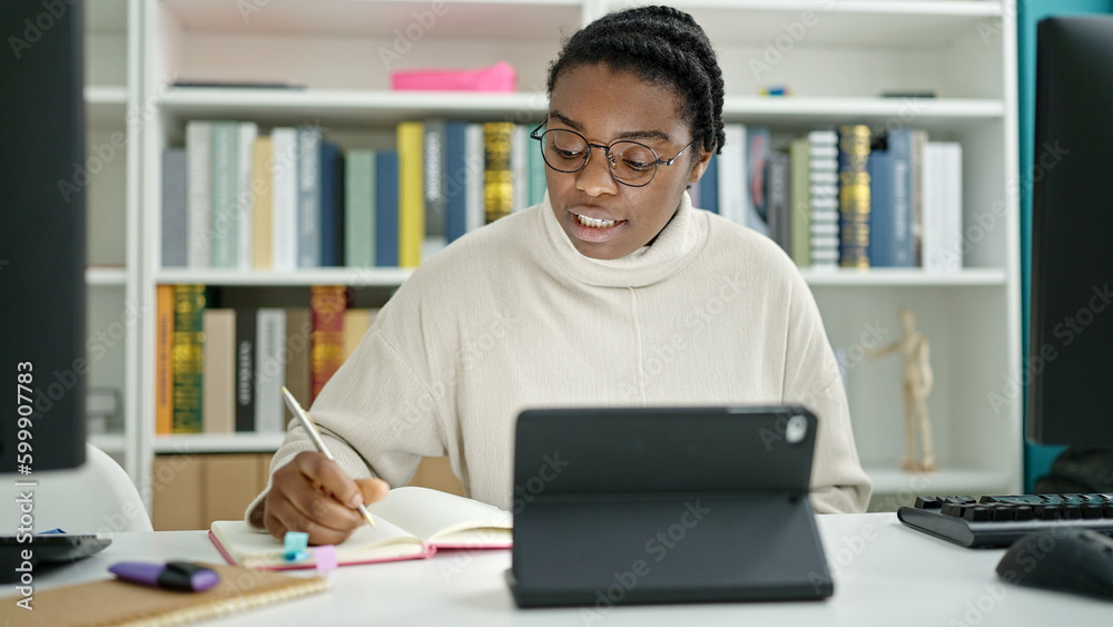 African american woman student using touchpad writing notes at library university African american woman student using touchpad writing notes at library university