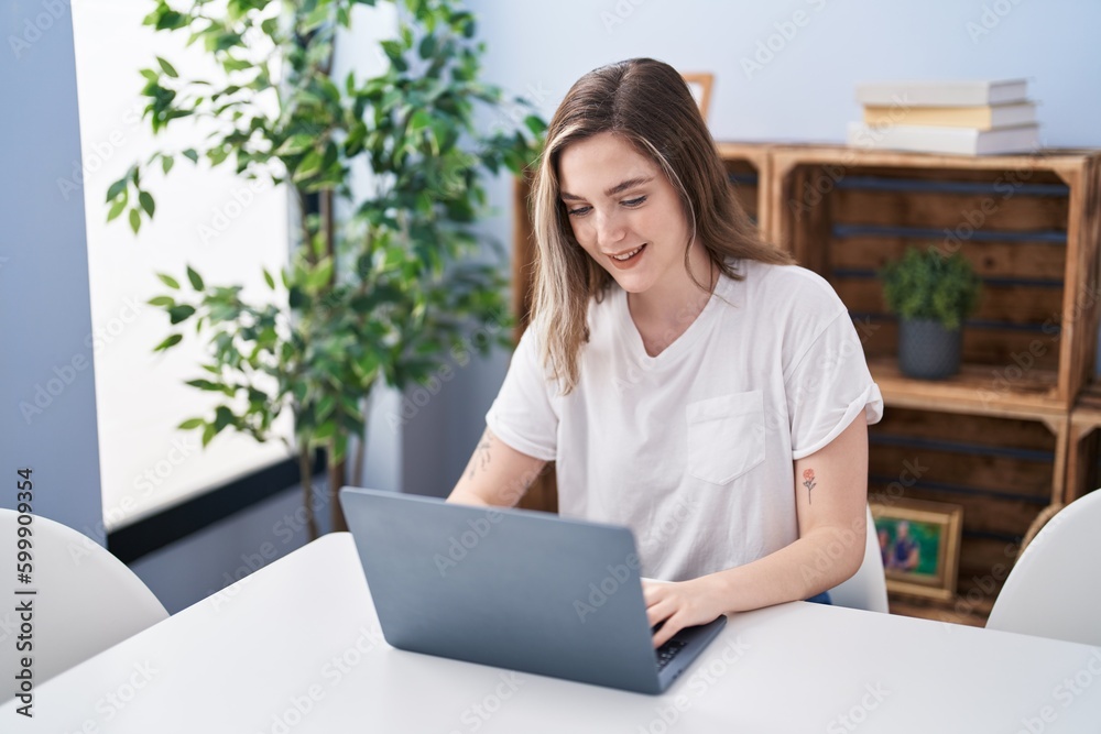 Young woman using laptop sitting on table at home Young woman using laptop sitting on table at home