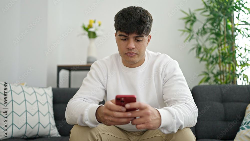 Young hispanic man using smartphone sitting on sofa at home Young hispanic man using smartphone sitting on sofa at home
