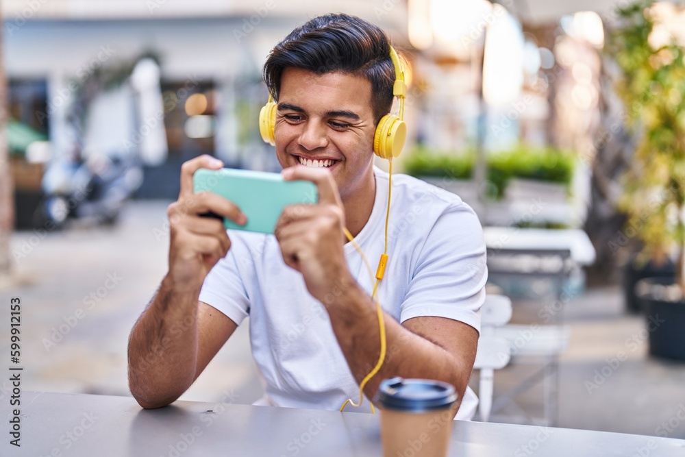 Young hispanic man playing video game drinking coffee at coffee shop terrace Young hispanic man playing video game drinking coffee at coffee shop terrace