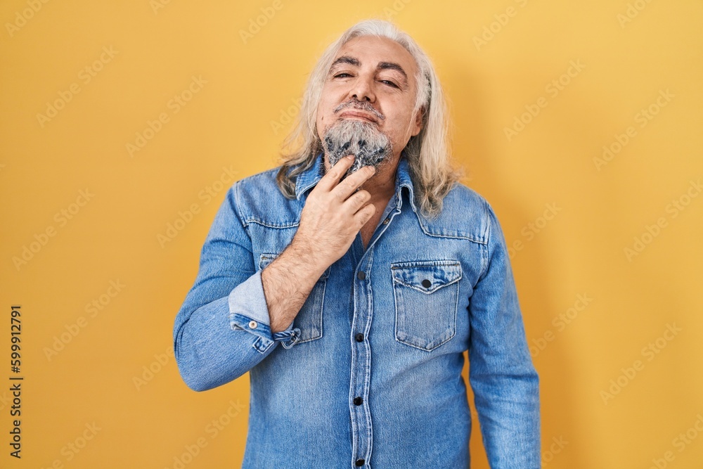 Middle age man with grey hair standing over yellow background thinking concentrated about doubt with finger on chin and looking up wondering Middle age man with grey hair standing over yellow background thinking concentrated about doubt with finger on chin and looking up wondering