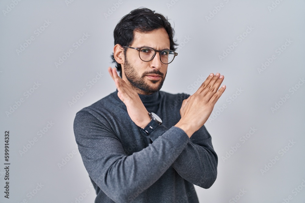 Obraz premium Handsome latin man standing over isolated background rejection expression crossing arms doing negative sign, angry face
