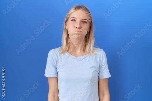 Young caucasian woman wearing casual blue t shirt puffing cheeks with funny face. mouth inflated with air, crazy expression. © Krakenimages.com