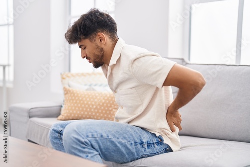 Young arab man suffering for backache sitting on sofa at home