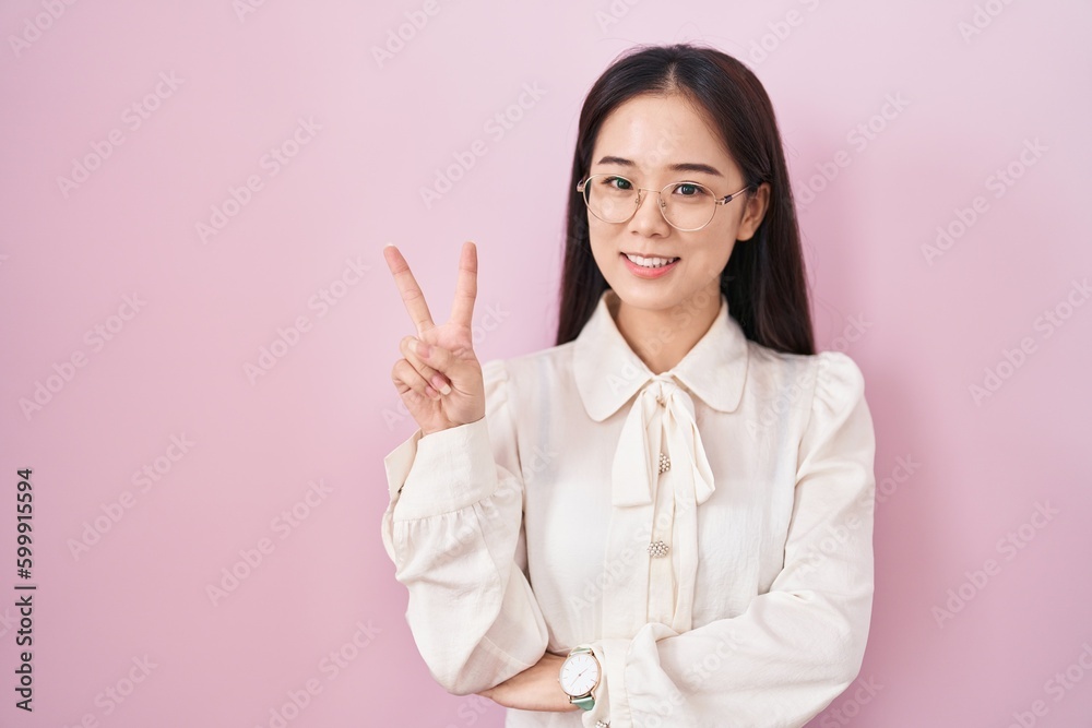 Young chinese woman standing over pink background smiling with happy face winking at the camera doing victory sign. number two. Young chinese woman standing over pink background smiling with happy face winking at the camera doing victory sign. number two.