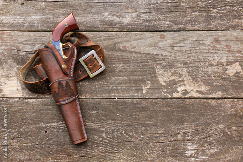 Black powder revolver in a leather holster with a leather belt on the background of old, worn boards. photo