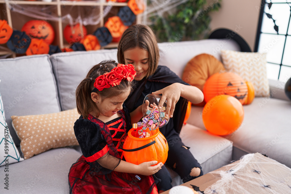 Fototapeta premium Adorable boy and girl having halloween party putting candies in pumpkin basket at home