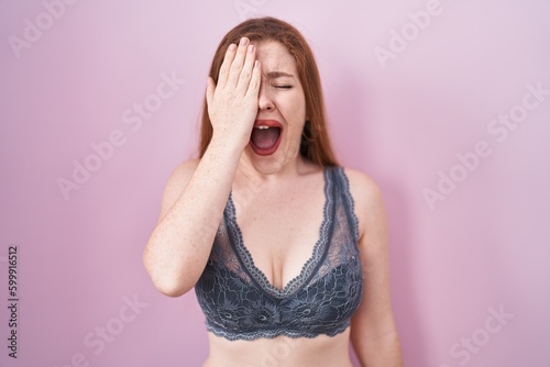 Redhead woman wearing lingerie over pink background yawning tired covering half face, eye and mouth with hand. face hurts in pain.