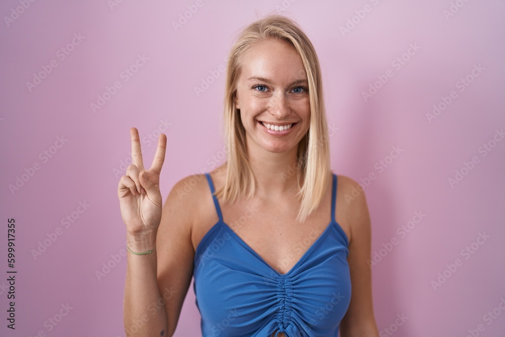 Young caucasian woman standing over pink background showing and pointing up with fingers number two while smiling confident and happy. Young caucasian woman standing over pink background showing and pointing up with fingers number two while smiling confident and happy.