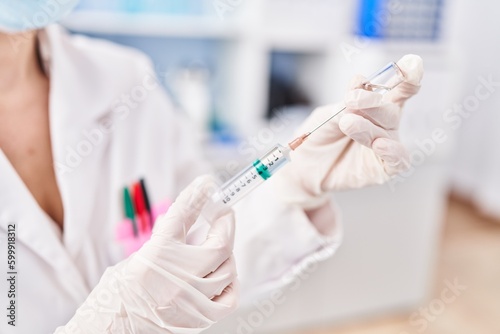 Young blonde woman scientist holding covid-19 vaccine at laboratory