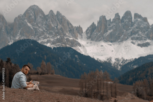 A man sits on a hill in front of a mountain with the mountains in the background. Hiking in the mountains. The alps.