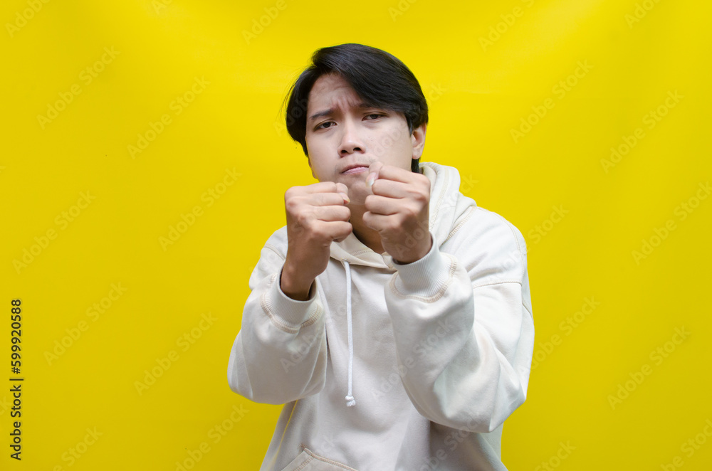 Obraz premium an Asian young man in beige hoodie, threatening, accusing, and looking for fight. A hysterical, mad depressed indonesian young man hand, shouts and screams loudly.