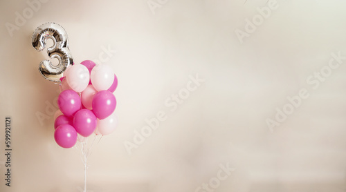 pink balloons backgroound with number 3 silver balloon on a beige background and space for texting or greeting. 