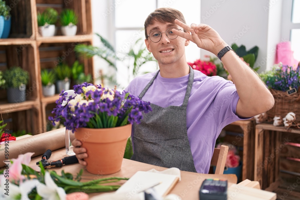 Caucasian blond man working at florist shop doing peace symbol with fingers over face, smiling cheerful showing victory