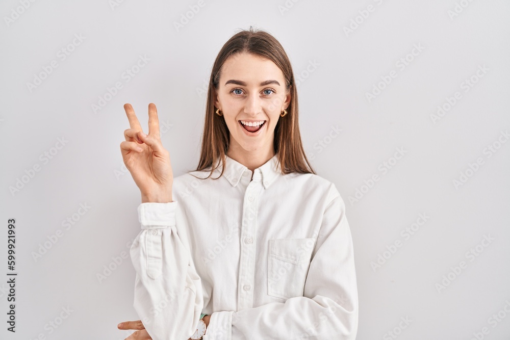 Young caucasian woman standing over isolated background smiling with happy face winking at the camera doing victory sign with fingers. number two. Young caucasian woman standing over isolated background smiling with happy face winking at the camera doing victory sign with fingers. number two.