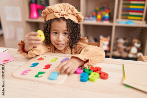 African american girl playing with maths puzzle game sitting on table at kindergarten