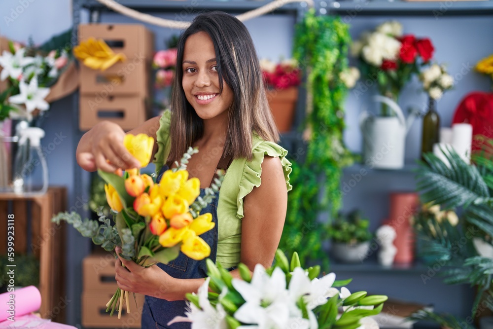 Young hispanic woman florist holding bouquet of flowers at florist store