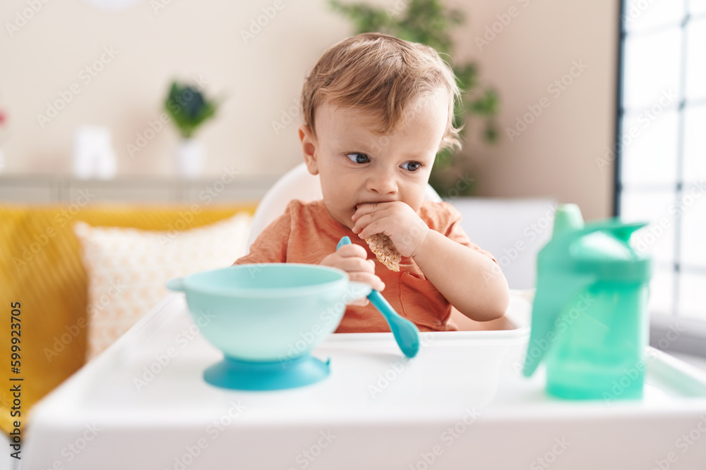 Adorable blond toddler sitting on highchair eating snack at home Adorable blond toddler sitting on highchair eating snack at home