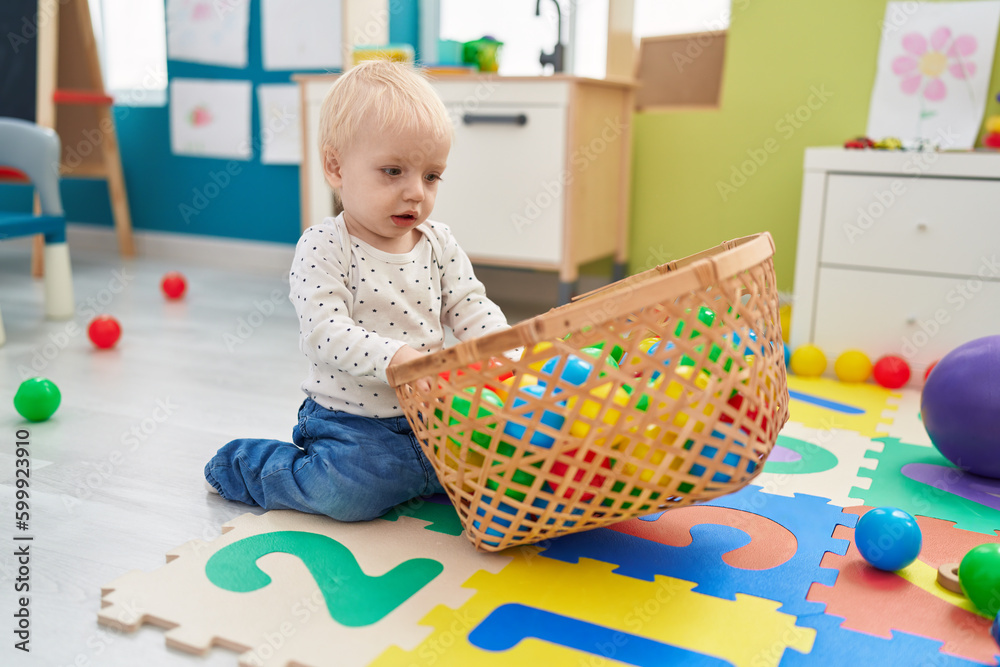Adorable blond toddler playing with balls sitting on floor at kindergarten Adorable blond toddler playing with balls sitting on floor at kindergarten