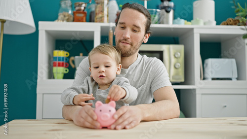 Fotografía Father and son inserting coin on piggy bank sitting on table at dinning room