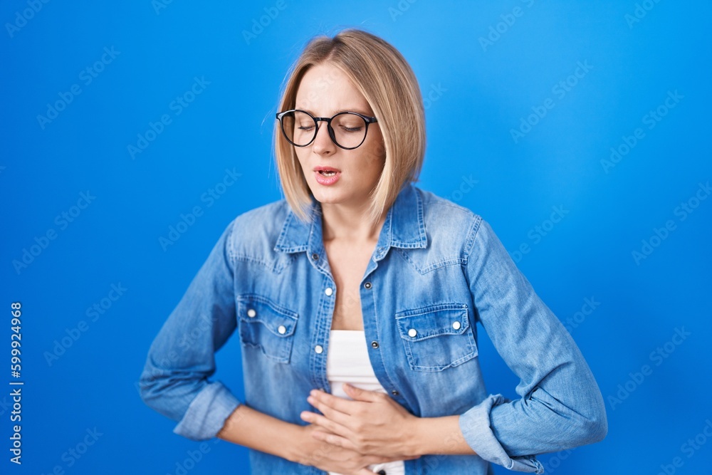 Young caucasian woman standing over blue background with hand on stomach because indigestion, painful illness feeling unwell. ache concept. Young caucasian woman standing over blue background with hand on stomach because indigestion, painful illness feeling unwell. ache concept.