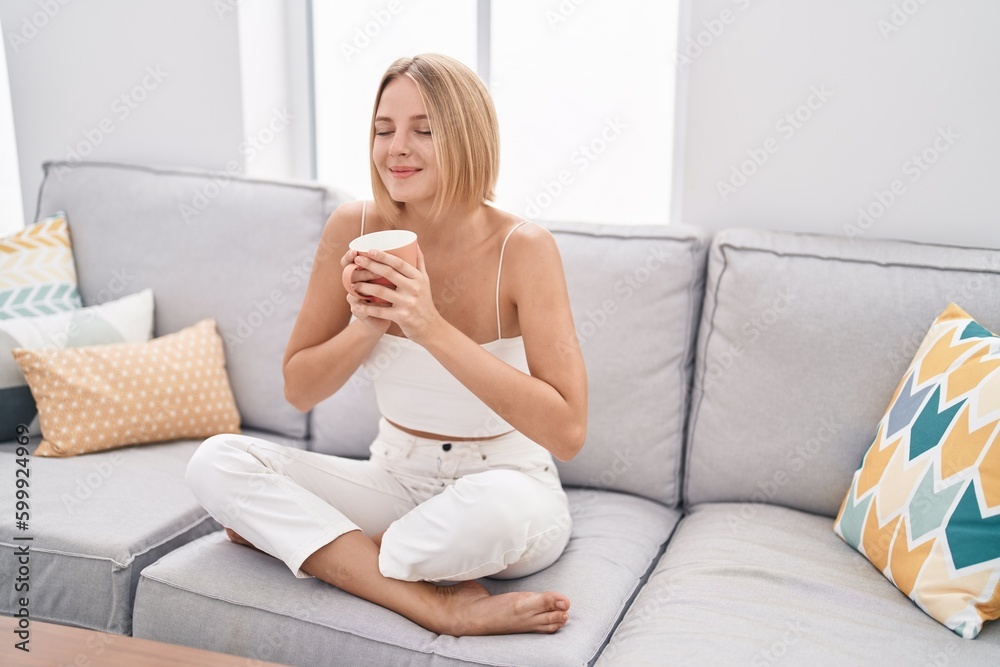 Young blonde woman drinking coffee sitting on sofa at home Young blonde woman drinking coffee sitting on sofa at home