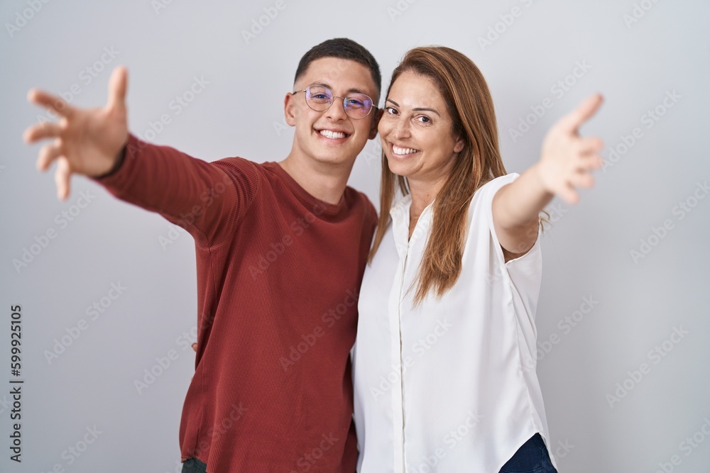 Mother and son standing together over isolated background looking at the camera smiling with open arms for hug. cheerful expression embracing happiness. Mother and son standing together over isolated background looking at the camera smiling with open arms for hug. cheerful expression embracing happiness.