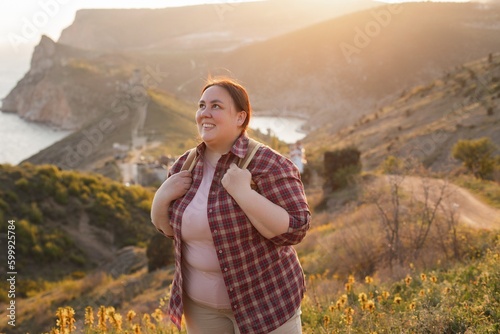 A plump woman enjoys the sunset. A tourist stands on top of a mountain and looks at the sunset.