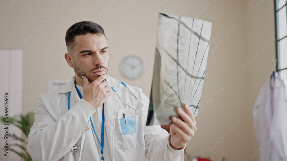 Young hispanic man doctor looking xray with doubt expression at clinic