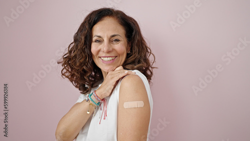 Foto Middle age hispanic woman smiling confident standing with band aid on arm over i