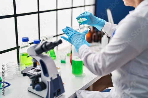 Middle age woman scientist pouring liquid on test tube at laboratory
