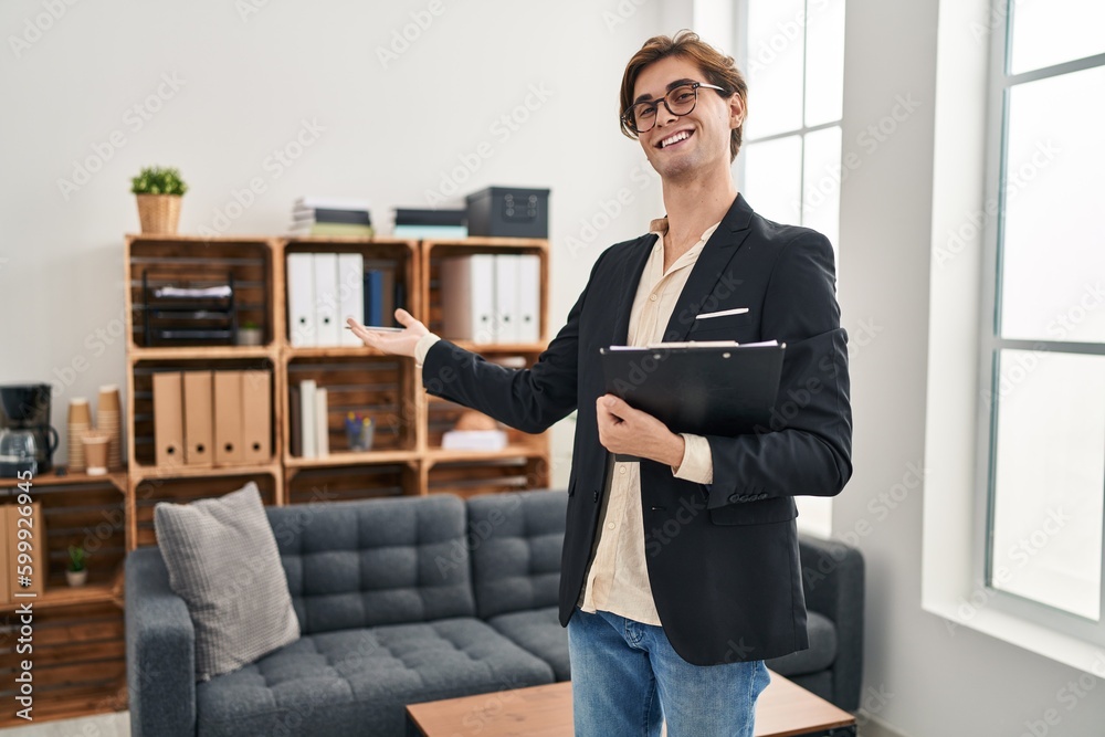 Young caucasian man business worker holding clipboard doing welcome gesture at office Young caucasian man business worker holding clipboard doing welcome gesture at office