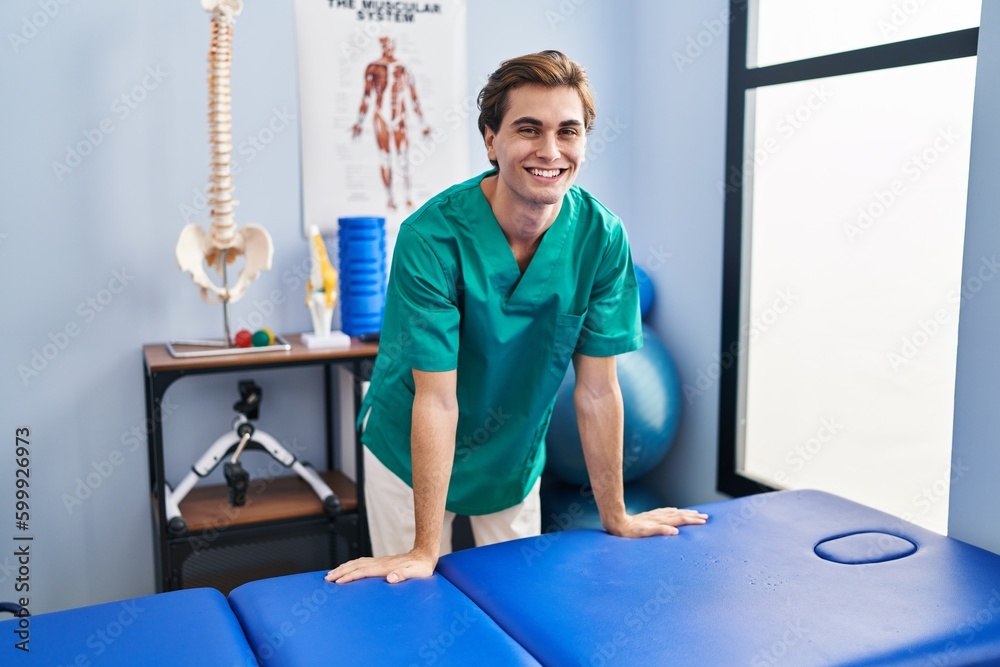 Young caucasian man pysiotherapist smiling confident standing at rehab clinic