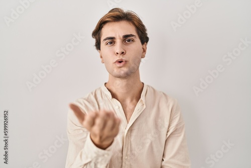 Young man standing over isolated background looking at the camera blowing a kiss with hand on air being lovely and sexy. love expression.