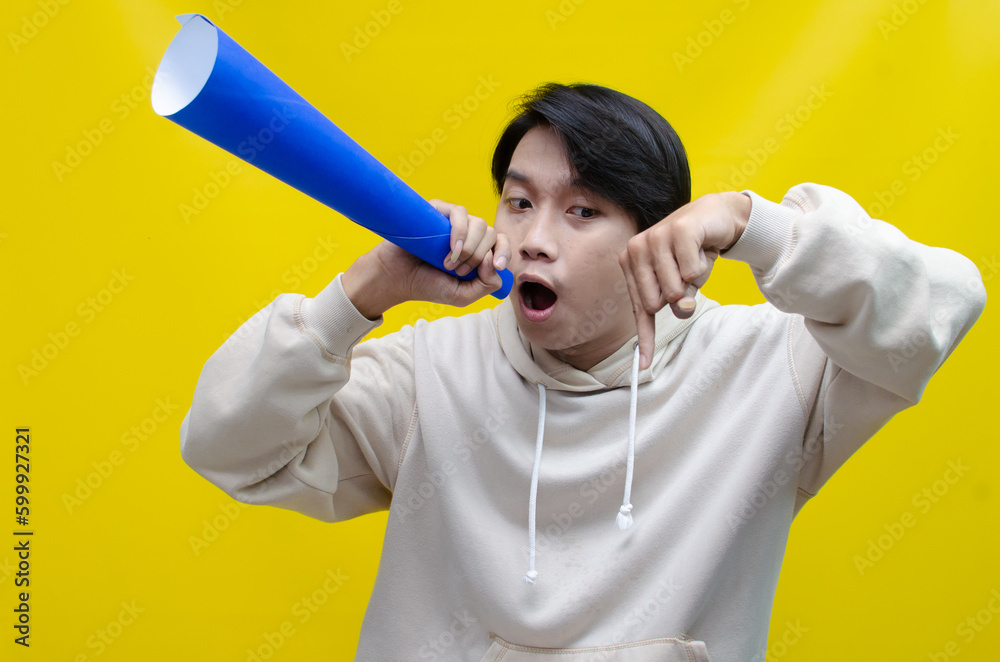 An ecstatic young Asian man in a cream hoodie whispering and shouting through a paper megaphone giving an announcement. asian man dancing and singing happily using paper as a megaphone.
An ecstatic young Asian man in a cream hoodie whispering and shouting through a paper megaphone giving an announcement. asian man dancing and singing happily using paper as a megaphone.