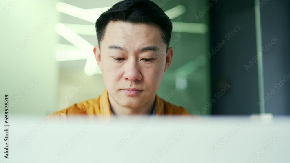 Close up. Thoughtful asian businessman working on a laptop and thinking about solving a problem, sitting at a workplace in a office. A serious entrepreneur analyzes and monitors the market situation Close up. Thoughtful asian businessman working on a laptop and thinking about solving a problem, sitting at a workplace in a office. A serious entrepreneur analyzes and monitors the market situation