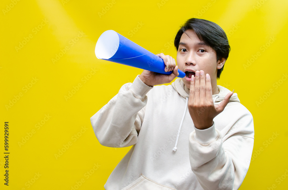 Shocked and surprised asian man shouting through paper megaphone giving an announcement. Shocked and surprised asian man shouting through paper megaphone giving an announcement.