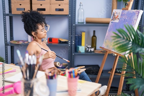 Young hispanic woman artist drawing with doubt expression at art studio