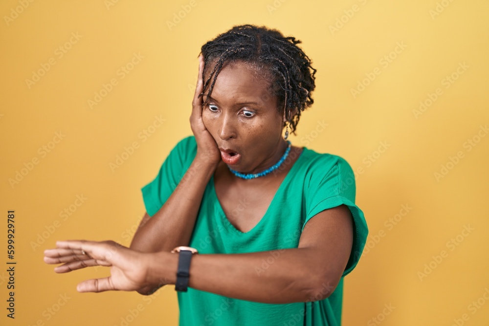 African woman with dreadlocks standing over yellow background looking at the watch time worried, afraid of getting late African woman with dreadlocks standing over yellow background looking at the watch time worried, afraid of getting late