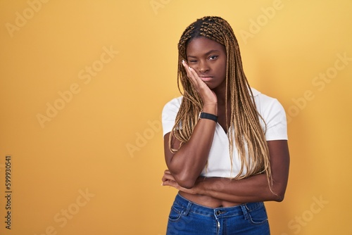 African american woman with braided hair standing over yellow background thinking looking tired and bored with depression problems with crossed arms.