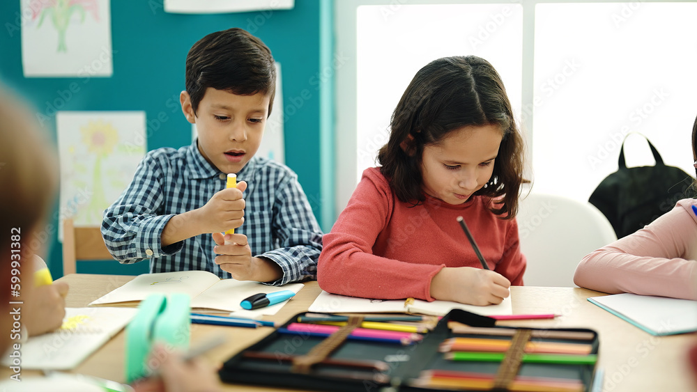 Adorable boy and girl students sitting on table drawing on notebook at classroom Adorable boy and girl students sitting on table drawing on notebook at classroom