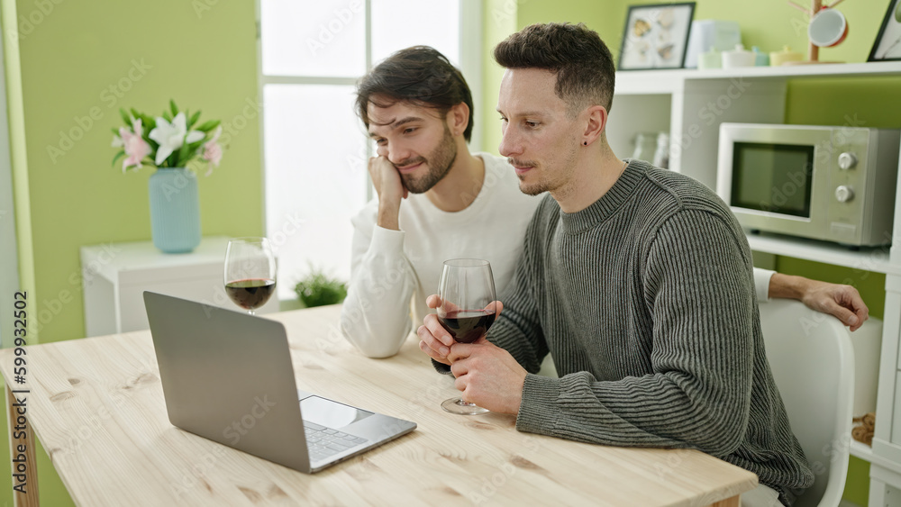 Two men couple watching movie drinking glass of wine at dinning room