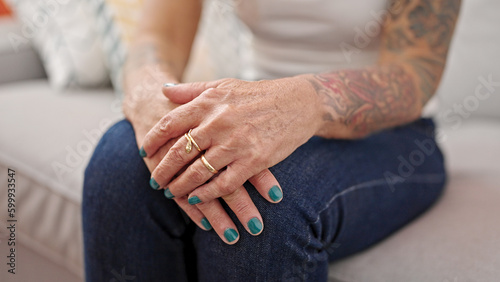 Middle age grey-haired woman sitting on sofa with hands together at home