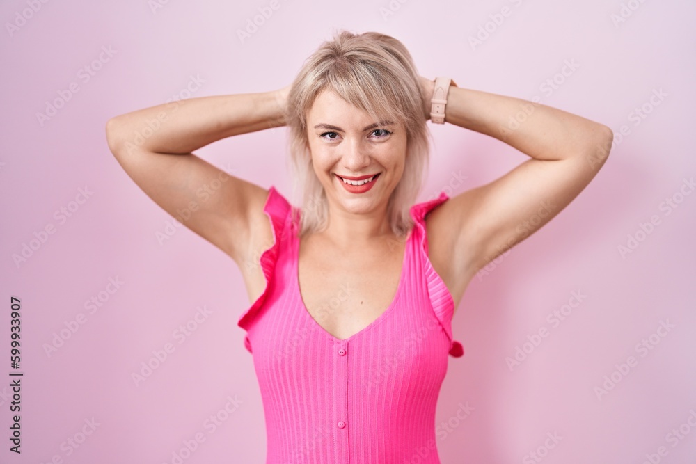 Young caucasian woman standing over pink background relaxing and stretching, arms and hands behind head and neck smiling happy Young caucasian woman standing over pink background relaxing and stretching, arms and hands behind head and neck smiling happy