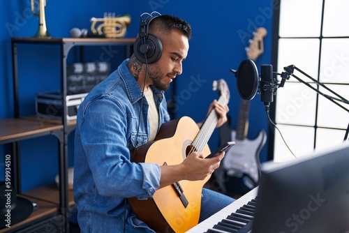 Young hispanic man artist using smartphone playing classical guitar at music studio